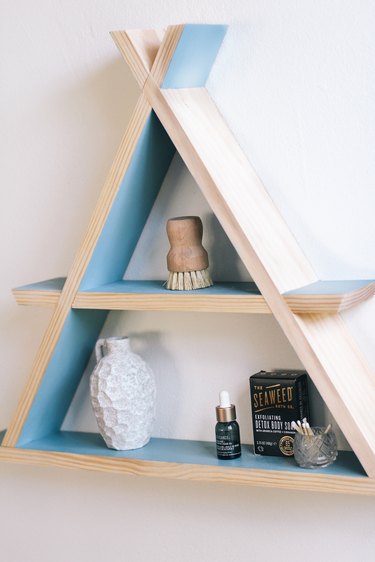 Wooden a-frame shelf with blue inner walls holding small containers on white wall