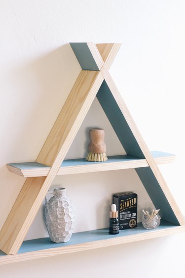 Wooden a-frame shelf with blue inner walls holding small containers on white wall