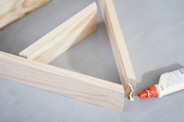 Glue bottle gluing together upper arch of wooden a-frame shelf against grey background