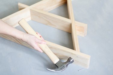 Hand hammering together wooden a-frame shelf against grey background