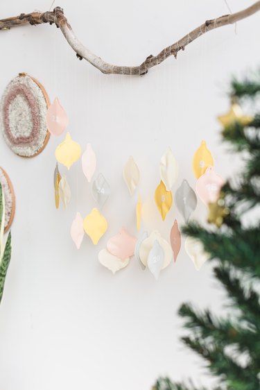a diy advent calendar with colorful hand-sewn numbered charms shaped like christmas lights, hanging from a tree branch