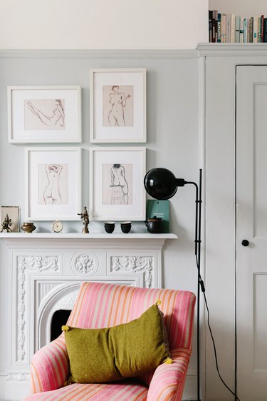White mantle against white wall with black potted candles, black lamp, and four white prints hung over mantle with pink couch in foreground
