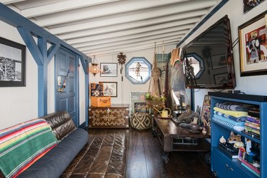 Living room with leather sofa, world decor, traditional textiles, tv, blue cabinets, and blue-white wall and ceiling beams.