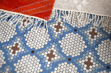 Small circle tiles in brown, white, and blue colors, forming a diamond and circle pattern. Edge of an orange rug.