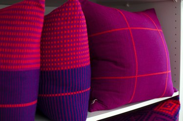 A shelf with fuchsia, red, purple pillows. Grid, striped, and square patterns.
