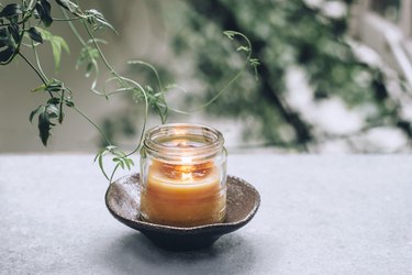 a diy beeswax candle burning in a glass jar on a saucer