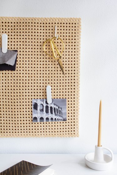 Cane memo board with scissors and photos over desk with candle