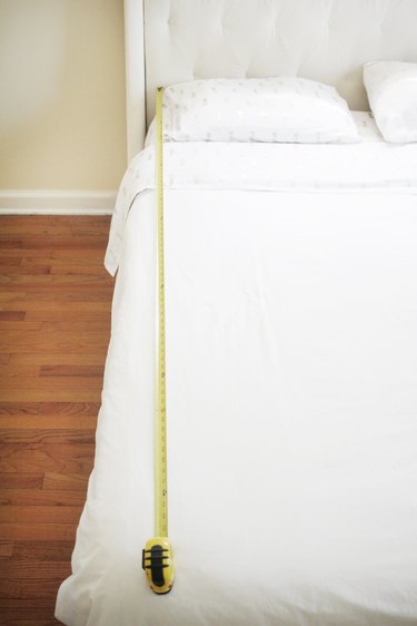 using a measuring tape to measure the length of an all-white bed