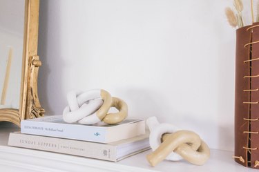 Decorative clay knots on mantel with books, leather vase and gold mirror