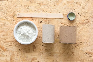 Paint mixer, wax, powder concrete, two cylindrical cardboard containers on wood tabletop