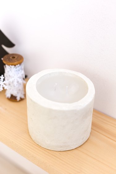 DIY concrete candle on wooden ledge next to snowflake string against white background