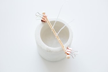 Two clips holding toothpics, upright wicks to concrete candle holder on white background