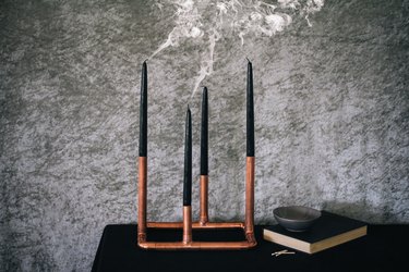 a candelabra made from copper pipe and four black taper candles