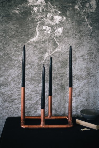 a candelabra made from copper pipe and four black taper candles