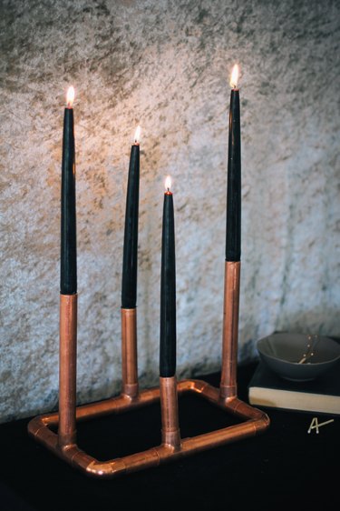 a candelabra made from copper pipe and four black taper candles