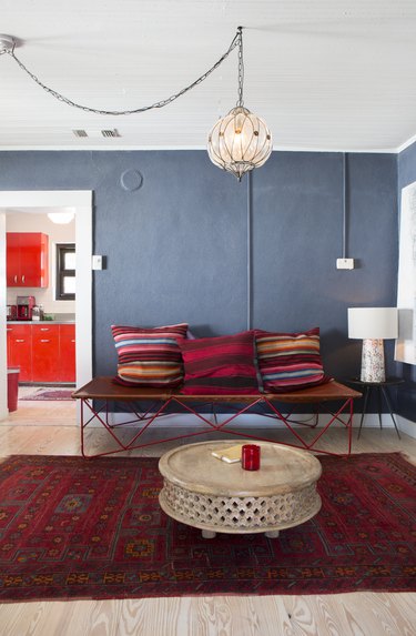 colors that go with red in a boho living room with gray walls, red rug, colorful pillows and globe pendant light