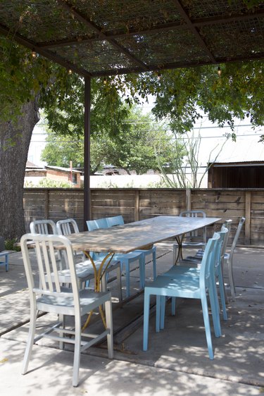 A wood dining table with white and blue chairs under a pergola