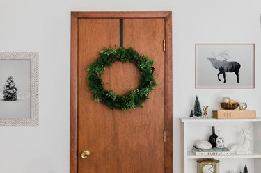 Christmas decor idea with faux evergreen wreath on wood door with framed art and white bookshelf