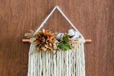 White yarn wall hanging with faux flowers and copper pipe