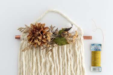 Thanksgiving door hanging with white yarn, faux flowers next to gold floral wire