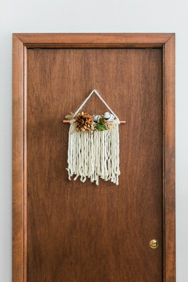 Thanksgiving door hanging with white yarn and faux flowers on wood door