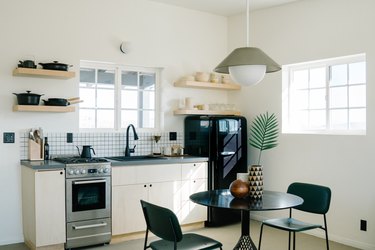A bold, minimalist kitchen with black dining furniture, wood shelves, white tile backsplash, and globe pendant light