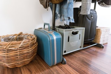 A wicker basket, vintage blue suitcase, crates, black suitcase by an open closet.
