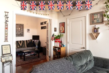 Living room with novelty bottles, plants, U.K. flags, and string light decor. A gray sofa, Southwestern textiles, and eclectic art.