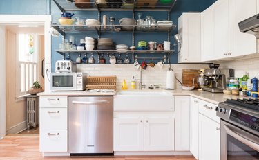Kitchen with white cabinets and blue walls. A white tile backsplash and wire shelving.