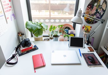 White desk with red notebook and closed laptop against window