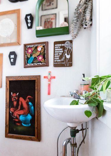 Boho bathroom with small white sink, trailing plant and gallery art wall.