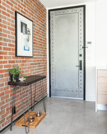Entryway with brick wall, white wall, metal doo, small entryway table, and hung framed print