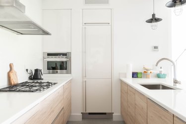 White contemporary kitchen with white countertops, wood cabinets, black stove burners, and silver sink and faucet