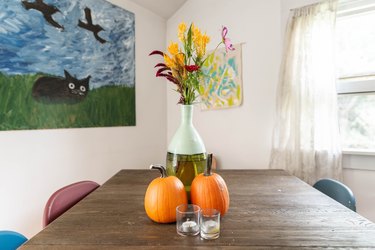 orange gourds, candles, and a bouquet of flowers form a centerpiece for a rustic dining room table