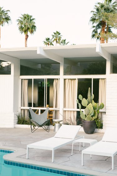 white chaise lounges on a pool deck with a butterfly chair and a large potted cactus