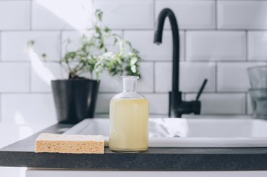 a glass bottle full of diy dish soap on a kitchen counter near the sink