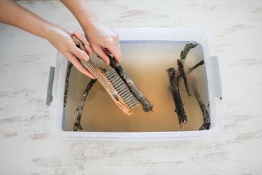 driftwood sticks are scrubbed in a basin with a stiff brush