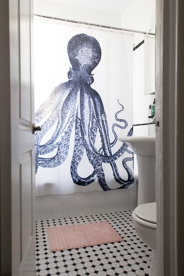 Shower curtain with a blue octopus, black-white floor tiles and a pink bathmat