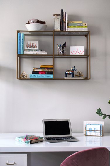 A white desk with a laptop and wall shelving with books