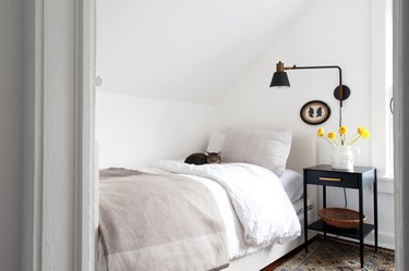 Bedroom with white bedding and walls with dark farmhouse lamp and nightstand