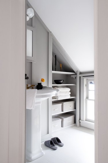 White-gray walled bathroom with built-in shelving for towels and slanted ceiling