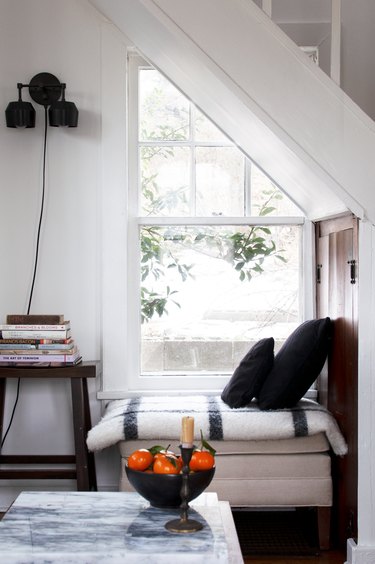 Reading nook with blanketed cushion and window with coffee table with oranges