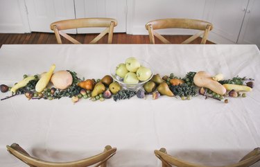 a line of produce, including grapes, pears, cherries, and squash runs down the length of a table with a white cloth