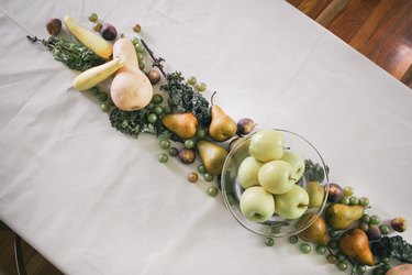 a line of produce, including grapes, pears, cherries, and squash runs down the length of a table with a white cloth