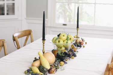 a line of produce, including grapes, pears, cherries, and squash runs down the length of a table with a white cloth