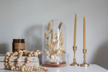 Cloche with dried plants next to candlesticks and wood bead necklace