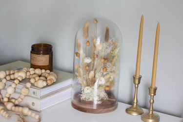 Cloche with dried plants next to candlesticks and wood bead necklace