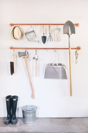 garage tools hanging on s-hooks that are suspended from copper pipes mounted on a wall
