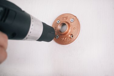 mounting spray-painted floor flanges on a wall with screws driven by a power drill