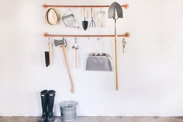 garage tools hanging on s-hooks that are suspended from copper pipes mounted on a wall